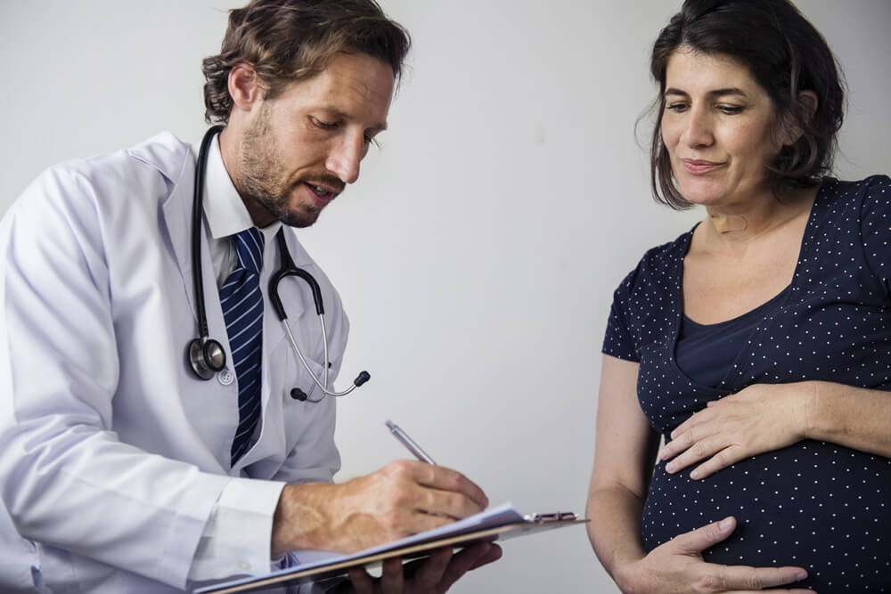 Perito ginecólogo recoge datos en su informe pericial mientras habla con una mujer embarazada
